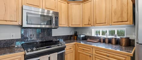 A kitchen with wooden cabinets, a stainless steel microwave, a gas stove, and a refrigerator.