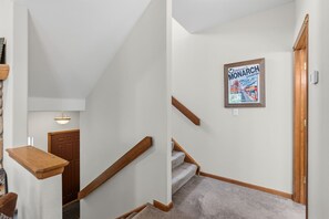 Un escalier avec des rampes en bois et des marches recouvertes de moquette, menant à un palier.