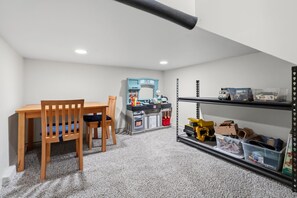 Une pièce avec une table et des chaises en bois, un coin cuisine équipé d’une cuisinière jouet et des étagères avec des bacs de rangement.