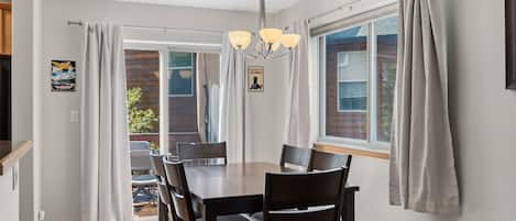 Un espace repas comprenant une table et des chaises, un lustre et des rideaux.