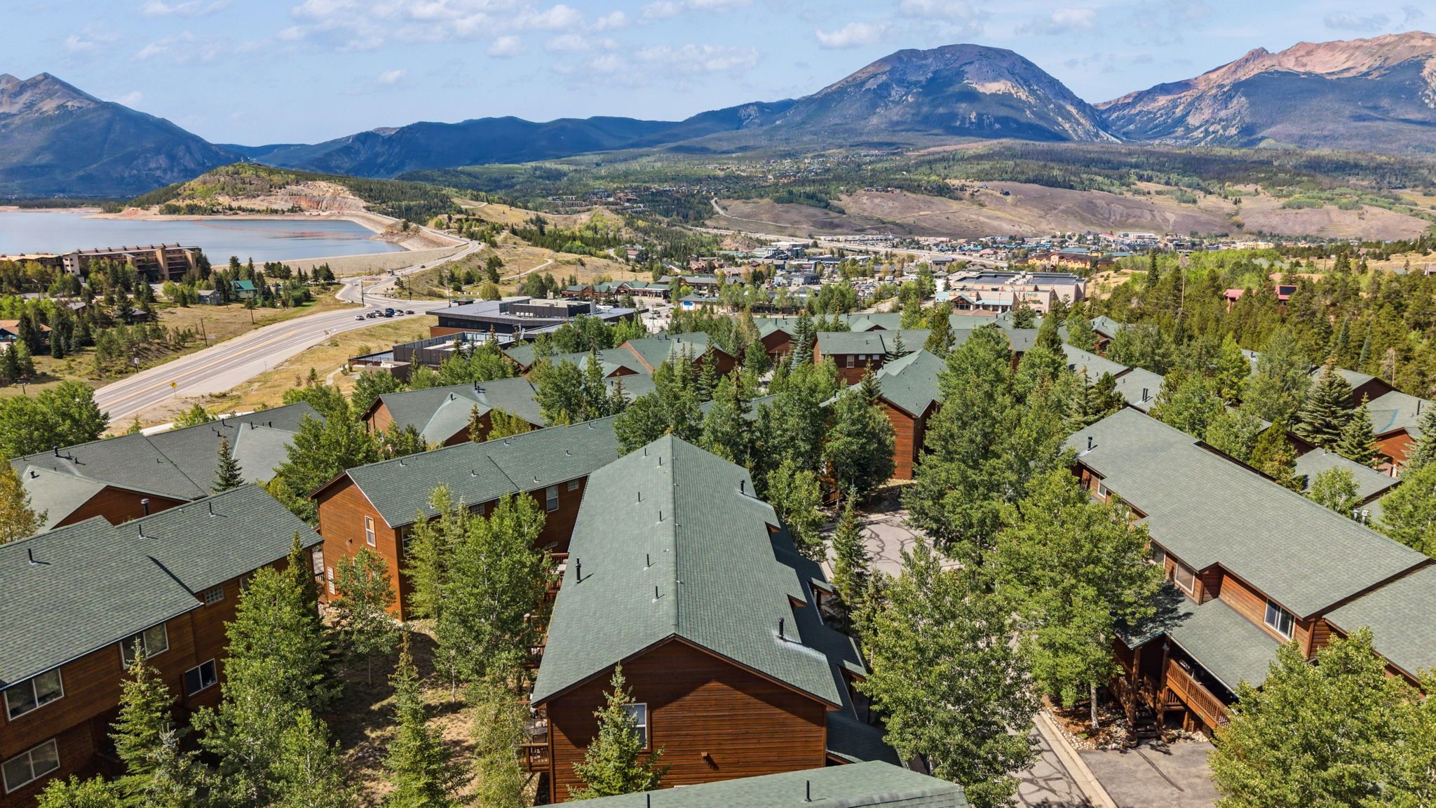 Un resort con varias cabañas rodeadas de árboles, un pueblo pequeño al fondo y montañas.