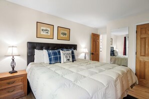 A bedroom with a large bed, two bedside tables, a nightstand, a wooden door, and a mirror. - New! Mountain Condo | Fireplace | Shared Hot Tub | 1 Mile to Purgatory Resort (Durango)