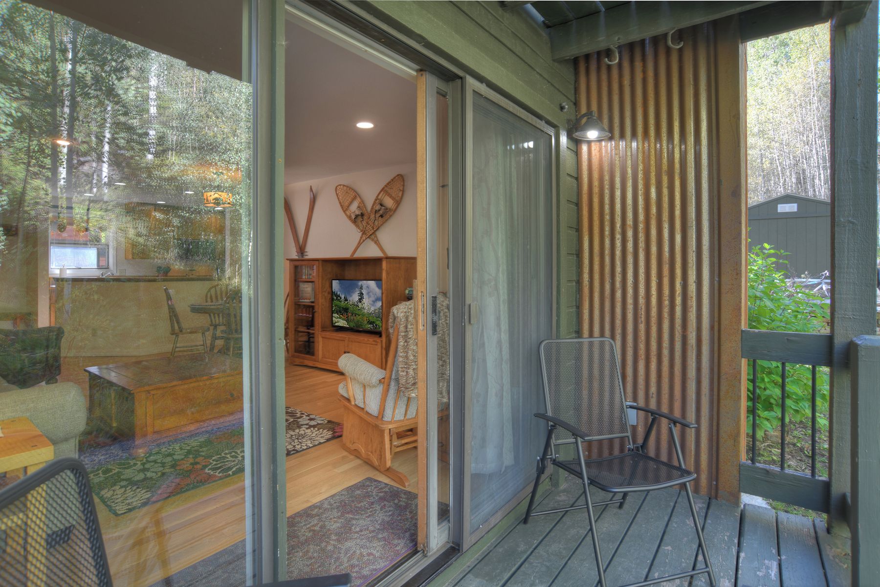 Ein Zimmer mit einer Schiebeglastür, die auf einen Balkon führt, einem Fernseher und einer Sitzecke mit einem gemusterten Teppich.