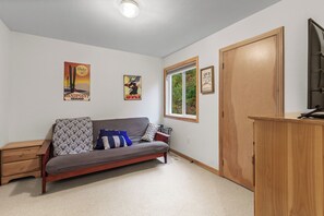 A room with a wooden cabinet, a sofa with patterned cushions, a wooden nightstand, and two posters on the wall. - New! Spacious Ski Retreat | Sleeps 13 | 3 Min to Schweitzer Mountain Resort (Sandpoint)