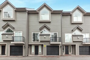 A row of townhouses with multiple garage doors, a central entrance with a door, and a small balcony on the second floor. - New! Spacious Ski Retreat | Sleeps 13 | 3 Min to Schweitzer Mountain Resort (Sandpoint)
