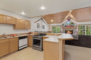 A kitchen with wooden cabinets, a stove, and a stone fireplace. - New! Spacious Ski Retreat | Sleeps 13 | 3 Min to Schweitzer Mountain Resort (Sandpoint)