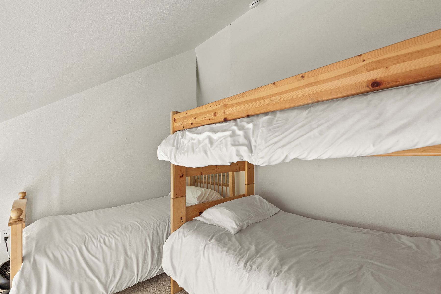 A bunk bed with white bedding in a room with white walls and a visible electrical outlet.