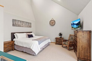 Ein Schlafzimmer mit einem Bett, einer Holzkommode, einem Sessel, einer Uhr und einem Gemälde an der Wand.