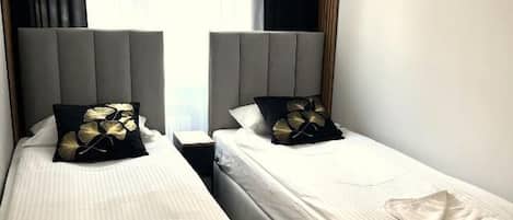 Two single beds with headboards, a window with curtains, and a wooden floor.