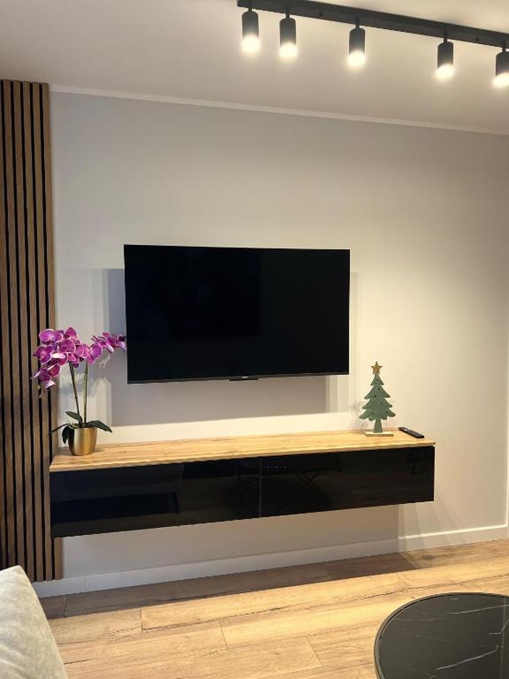 A modern living room with a mounted TV, a wooden console table, a small Christmas tree, and a potted orchid.