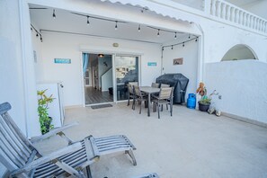 Um pátio externo com mesa e cadeiras, churrasqueira e um vaso de planta.