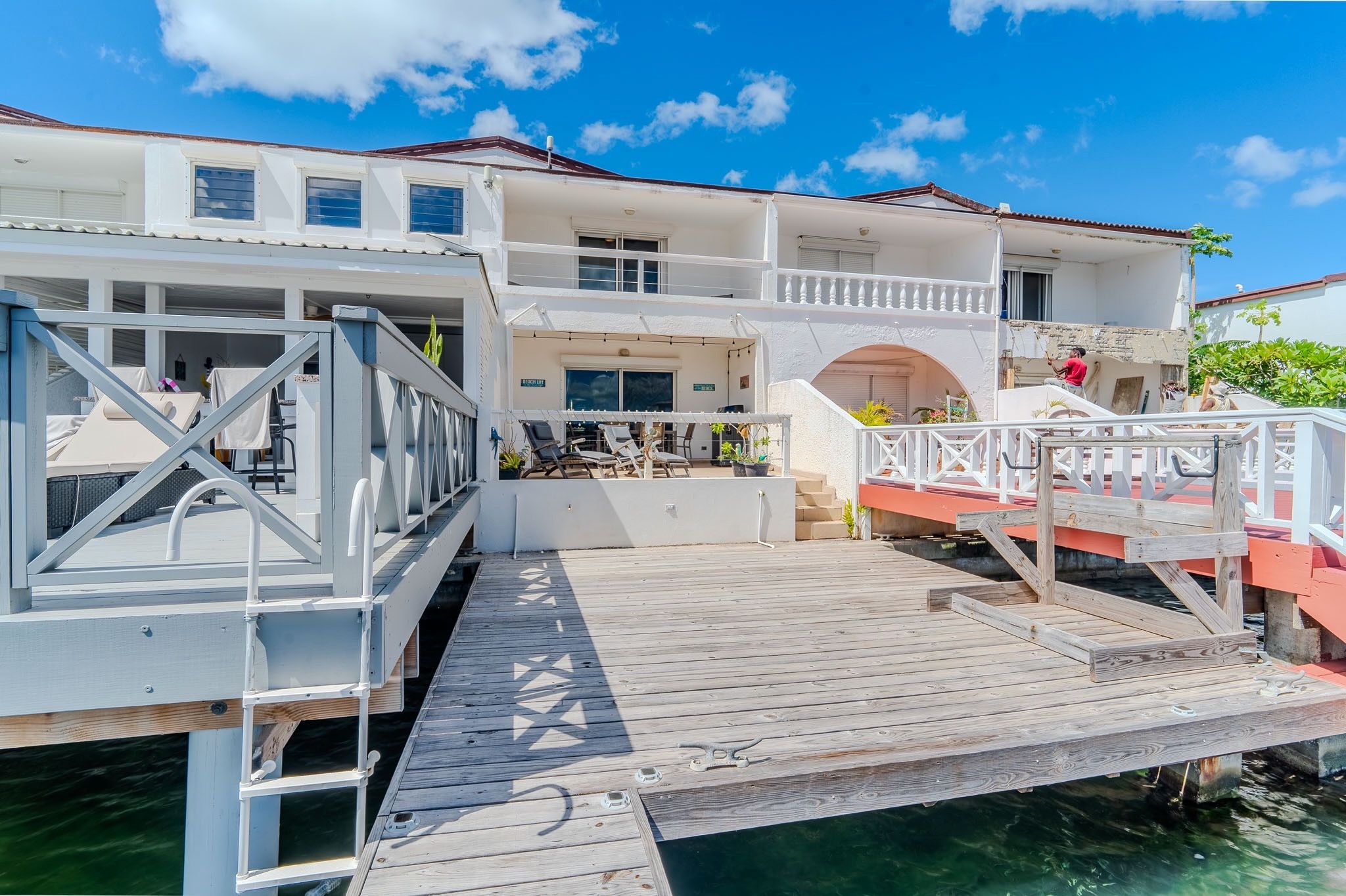 Une propriété située au bord de l’eau, avec une jetée en bois menant à une maison dotée de plusieurs balcons et d’un espace salon extérieur.