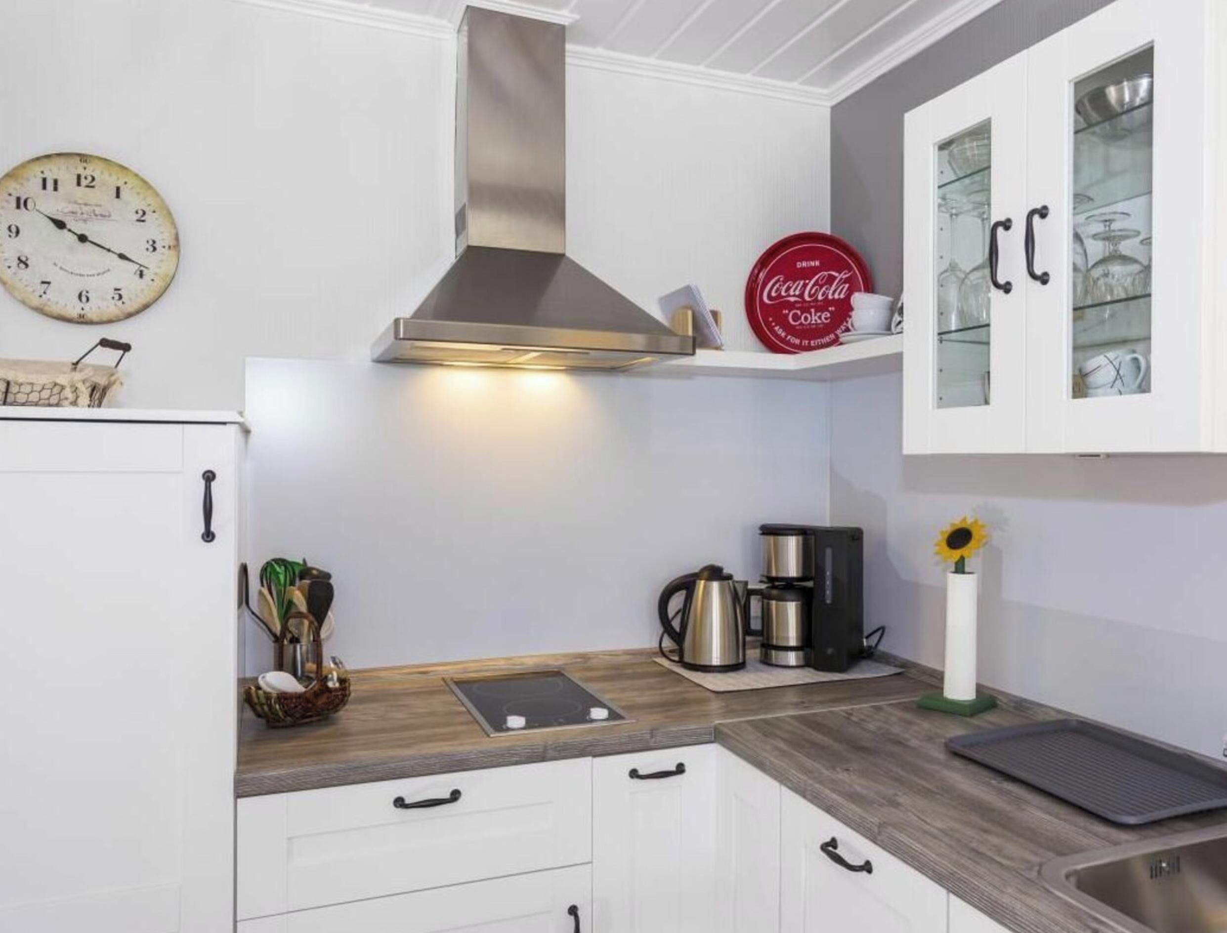 A kitchen with white cabinets, a stainless steel range hood, a clock, a Coca-Cola sign, and a coffee maker.