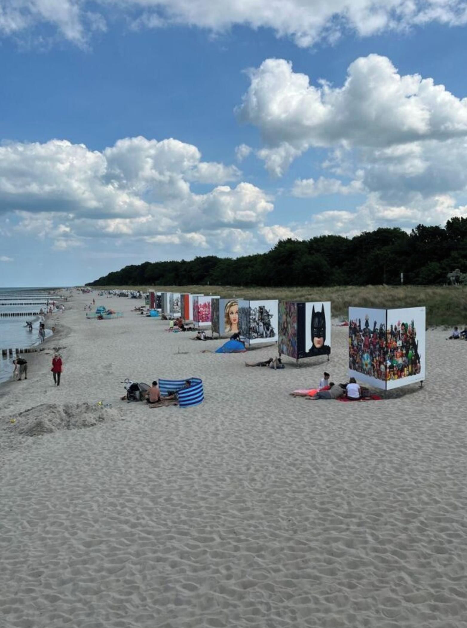 A beach with art installations and people walking.