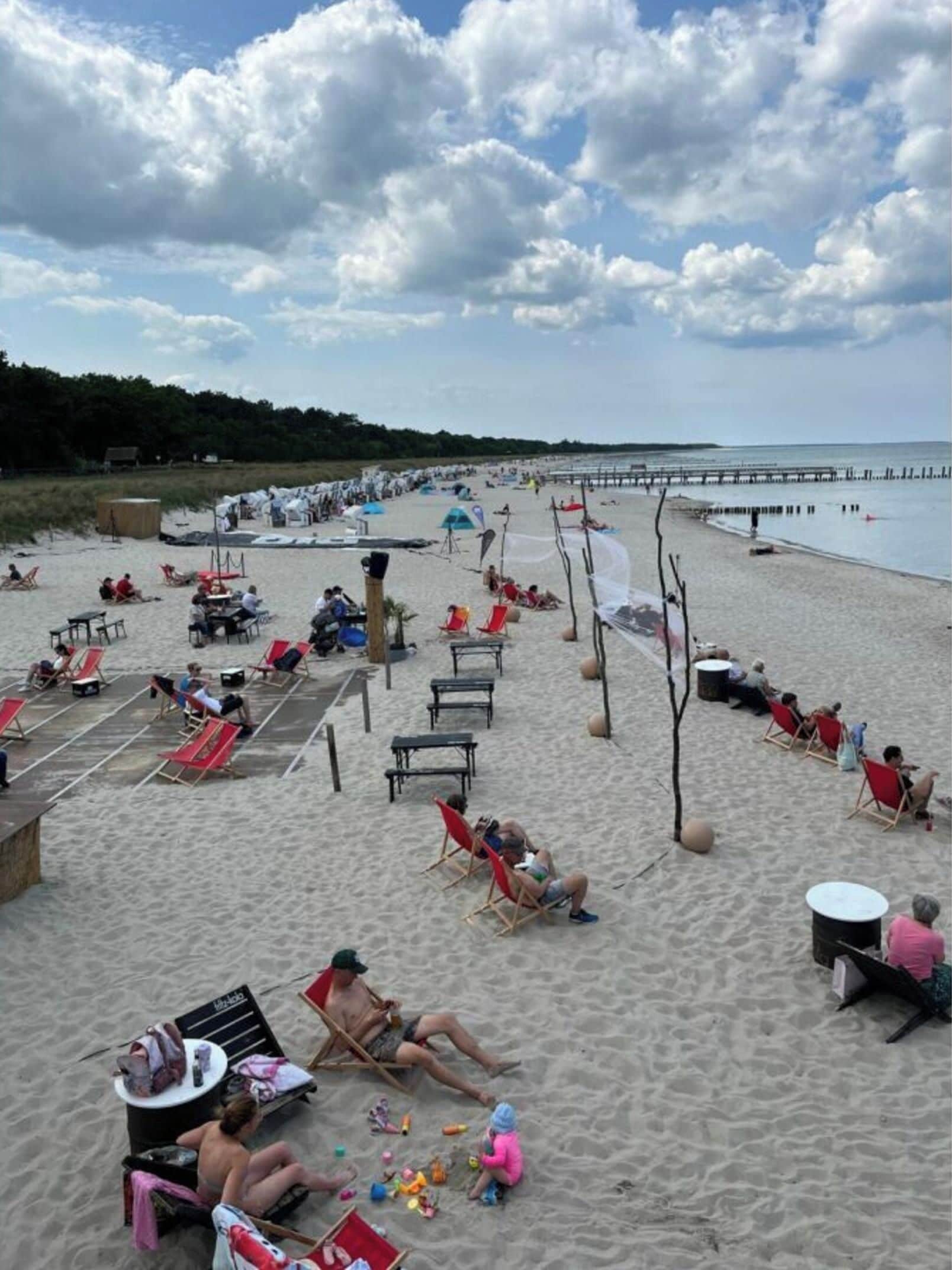 A beach with sun loungers, umbrellas, and a pier extending into the water.
