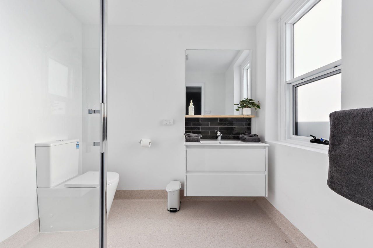 A modern bathroom with a glass shower enclosure, a toilet, a sink with a mirror above, and a window providing natural light.