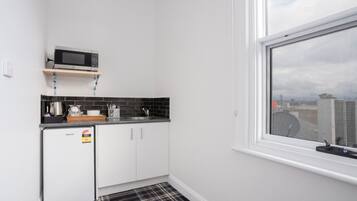 Une cuisine compacte avec un micro-ondes posé sur une étagère, un petit réfrigérateur et une fenêtre donnant sur la ville.