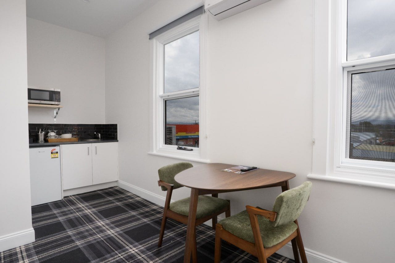 A compact kitchen with white cabinets, a microwave, and a small dining area with two chairs and a table.