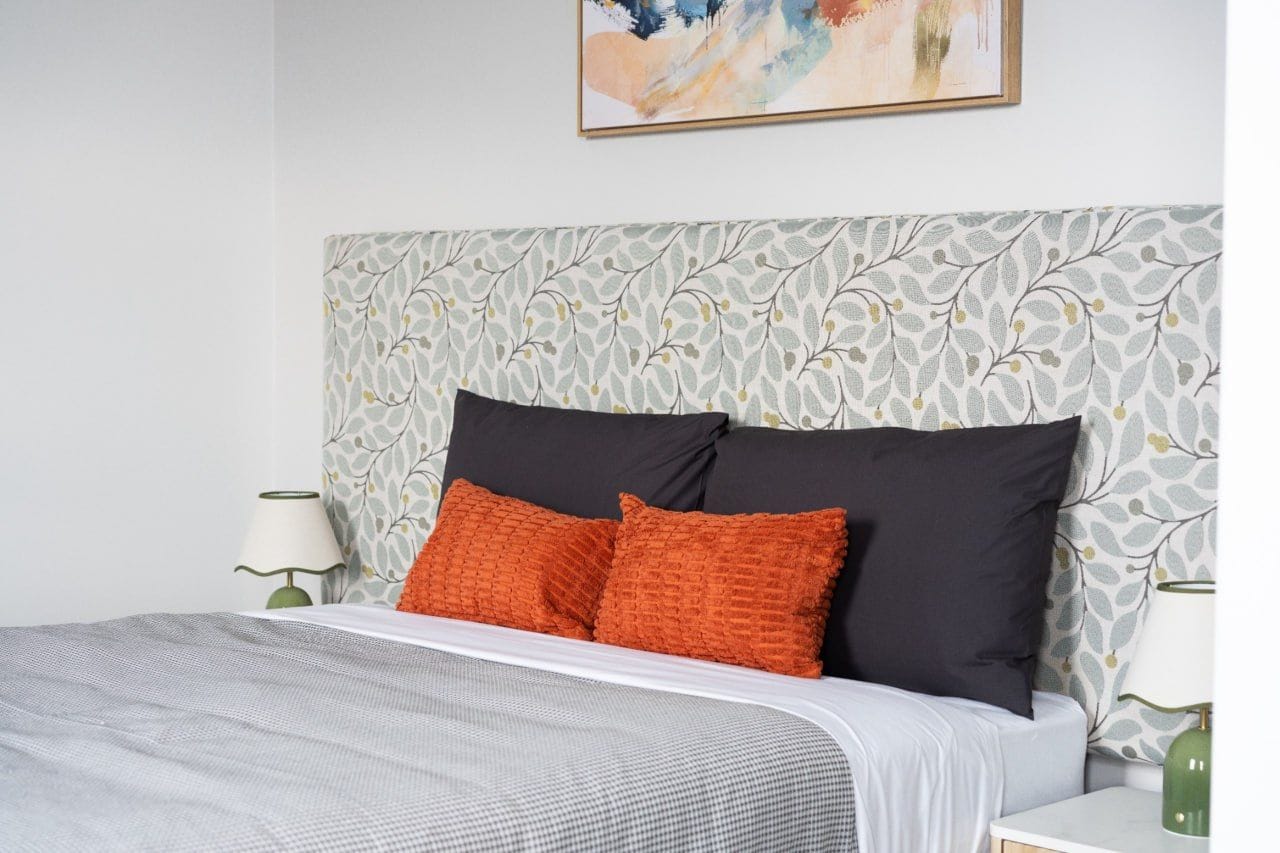 Una cama bien hecha con un cabecero estampado, dos almohadas y una mesita de noche con una lámpara.