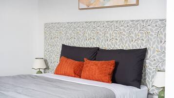 Una cama bien hecha con un cabecero estampado, dos almohadas y una mesita de noche con una lámpara.