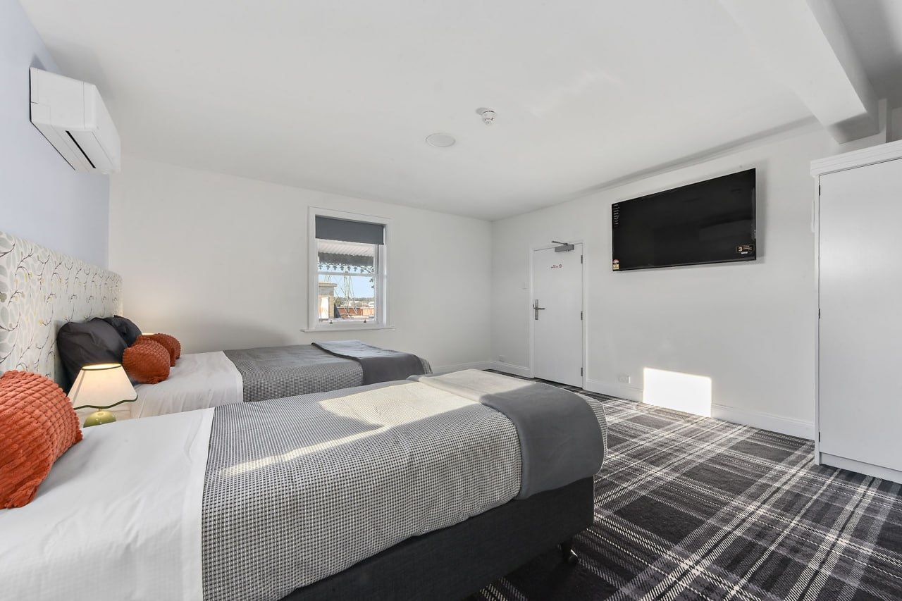 A hotel room with two beds, a television, a window, and a door.