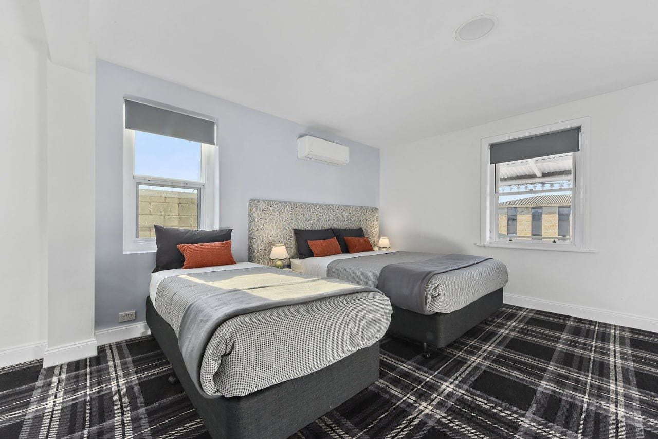 A bedroom with two beds, a headboard, a window, and a black and white checkered floor.