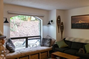 Un salón acogedor con un banco, un sofá, una mesa de centro y un amplio ventanal con vistas a un jardín.