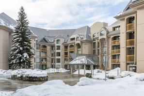 A multi-story building with balconies, a covered outdoor area, and a snow-covered landscape. - Upper Vill 1BR: Walk to Ski-In/Out, Sleeps 4! Hot Tub, Sauna & Gym. (Whistler)