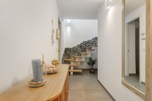 Ein Flur mit einem Holztisch, einer Glasvase mit Meeresschalen, einer Treppe mit einer Mosaikwand und einer Topfpflanze.