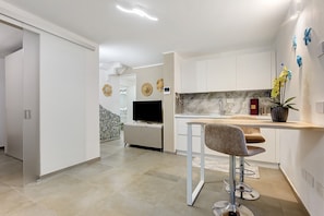 A modern kitchen with white cabinets, a built-in oven, and a dining area with a bar stool. - Villa Fonty by And Service with sea view, Wi-Fi and air conditioning (Golfo Aranci)