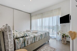 Ein modernes Schlafzimmer mit Bett, Vorhängen, einem Flachbildfernseher und einer Zierpflanze.