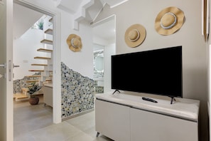 A modern interior with a flat-screen TV on a cabinet, a staircase with wooden steps, and two hats on the wall. - Villa Fonty by And Service with sea view, Wi-Fi and air conditioning (Golfo Aranci)