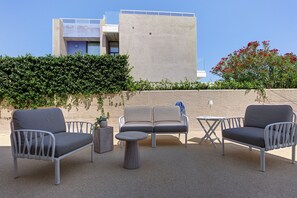 An outdoor seating area with two sofas, two armchairs, and a small table, set against a building with a concrete facade and a hedge in the foreground. - Villa Fonty by And Service with sea view, Wi-Fi and air conditioning (Golfo Aranci)
