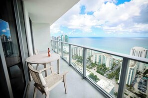 A balcony with a round table and chairs, overlooking a cityscape and the ocean. - 2-Bedroom Diamond In The Sky With Free Parking (Hollywood)