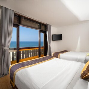 Habitación de hotel con dos camas, televisión y balcón con vista al mar.