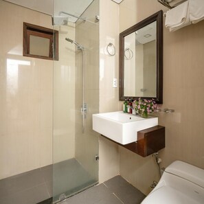 Un baño con cabina de ducha de vidrio, un lavamanos blanco con espejo y un inodoro.