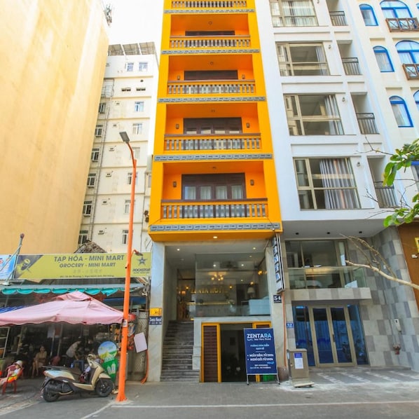 Un edificio de varios pisos con entrada a nivel de calle, una escalera visible y un cartel que indica el hotel ZENTARA.