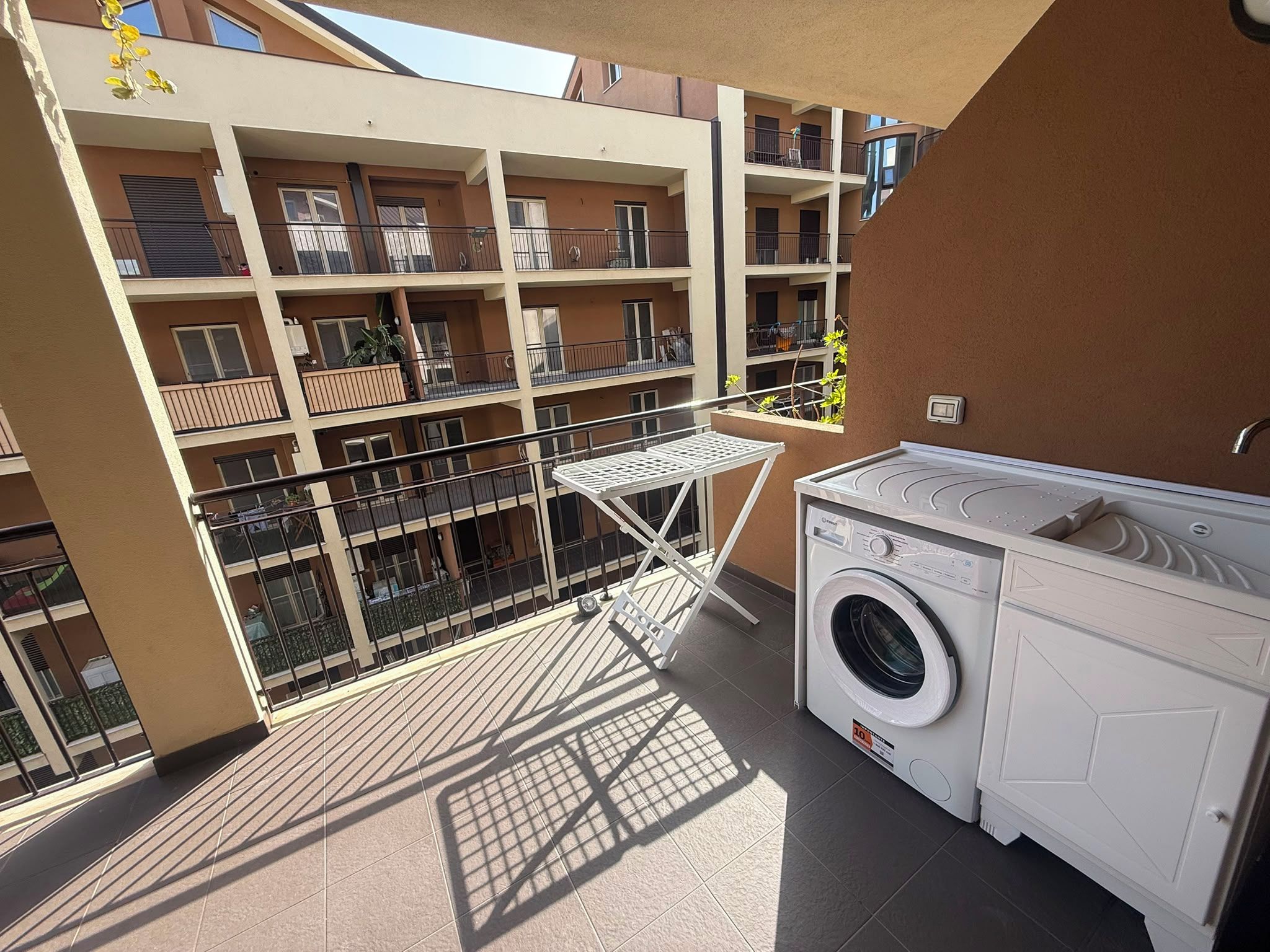 A balcony with a washing machine and a drying rack, surrounded by a multi-story building with balconies.