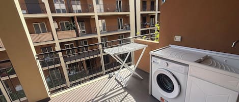 A balcony with a washing machine and a drying rack, surrounded by a multi-story building with balconies.