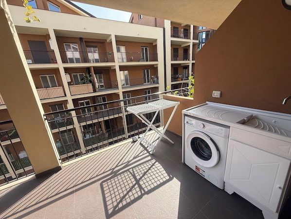 A balcony with a washing machine and a drying rack, surrounded by a multi-story building with balconies.