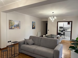 Ett modernt vardagsrum med en grå soffa, ett matbord och ett kök i bakgrunden.