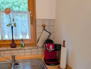 A kitchen with a sink, a window with a lace curtain, a vase with a flower, and a red coffee maker. - 2.3/t4 Holiday Park "freesenbruch" (Zingst)