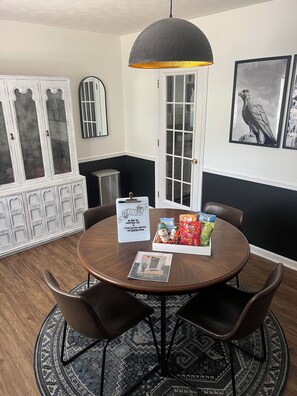 A dining area with a round table, two chairs, a pendant light, a cabinet with glass doors, and a framed artwork on the wall. - The Heritage Home, Walk to Downtown (Auburn)