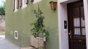 A building with a green exterior, a wooden bench, a potted plant, and a door with a number.