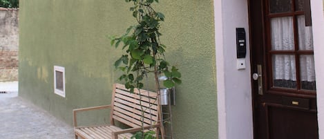 A building with a green exterior, a wooden bench, a potted plant, and a door with a number.