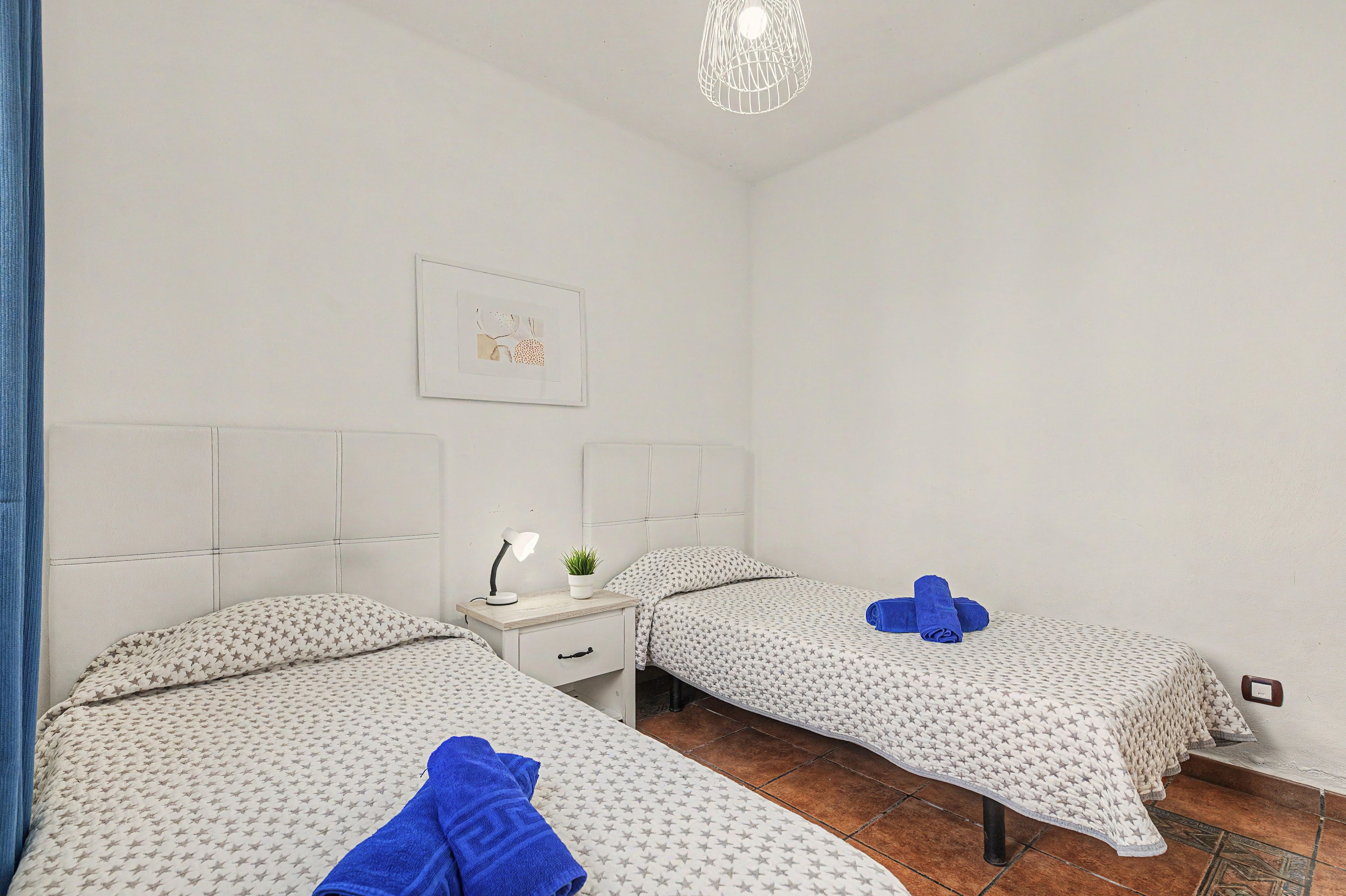 A hotel room with two beds, a nightstand, a wall-mounted lamp, and a small potted plant.