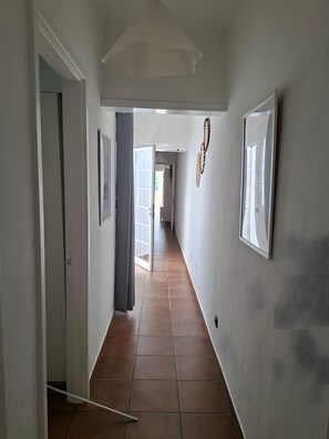 A hallway with a tiled floor, white walls, and a door on the left.