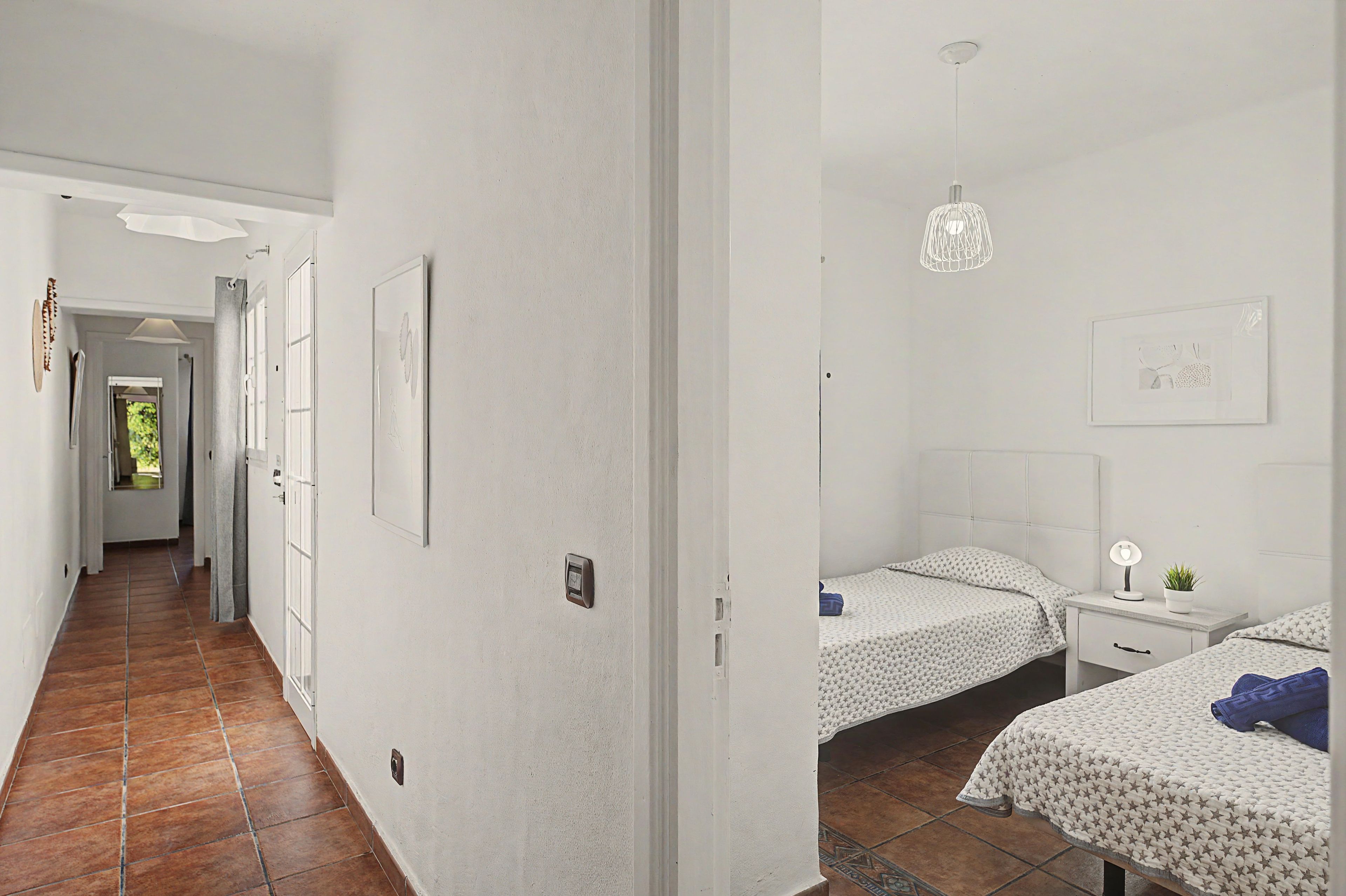 A hotel room with two beds, a nightstand, a lamp, and a hanging light fixture.