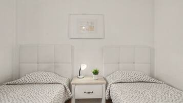 A twin room with two beds, a bedside table with a lamp, a small plant, and a framed picture on the wall.