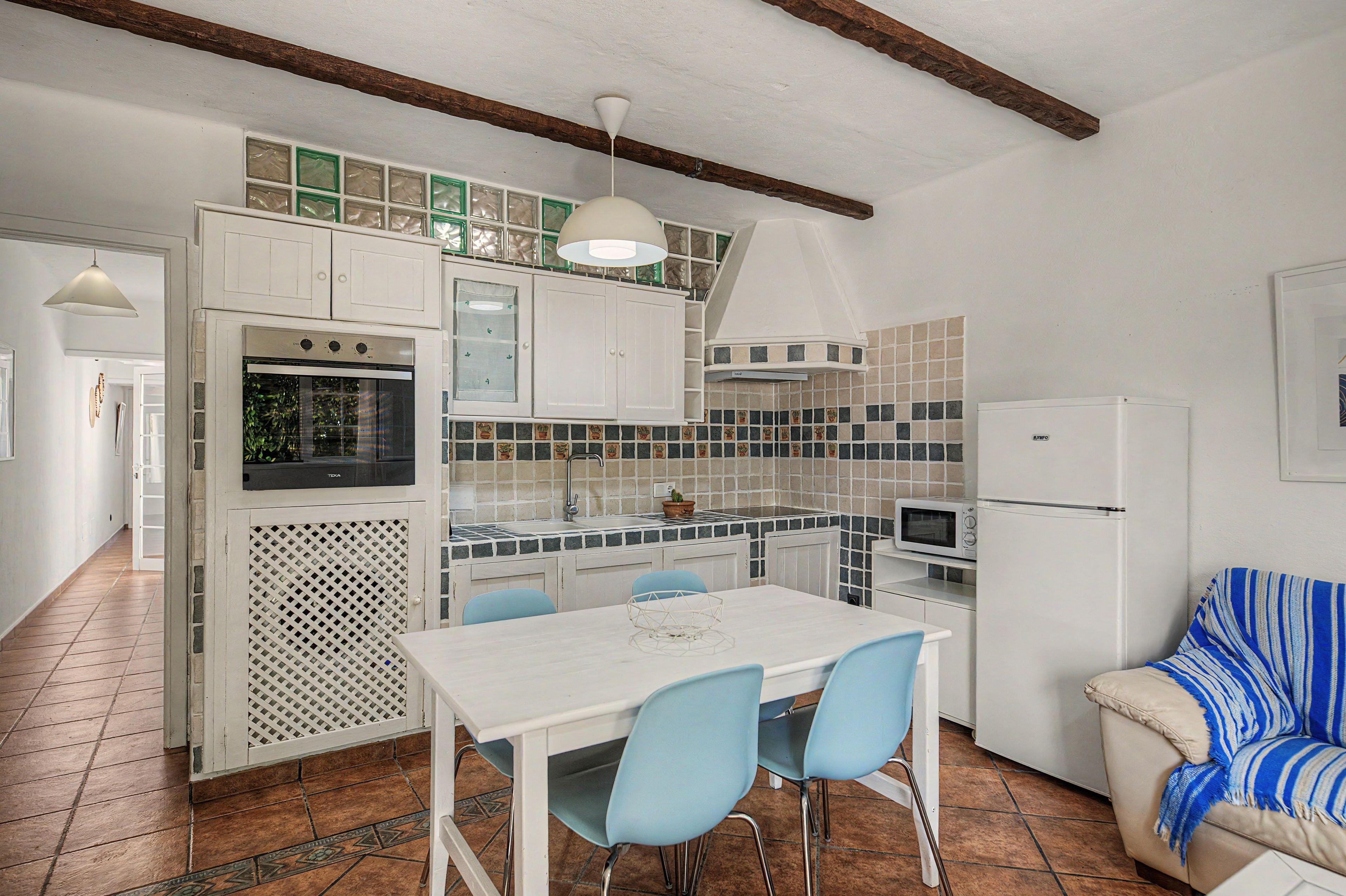 A compact kitchen with white cabinets, a dining table with chairs, a microwave, and a refrigerator.